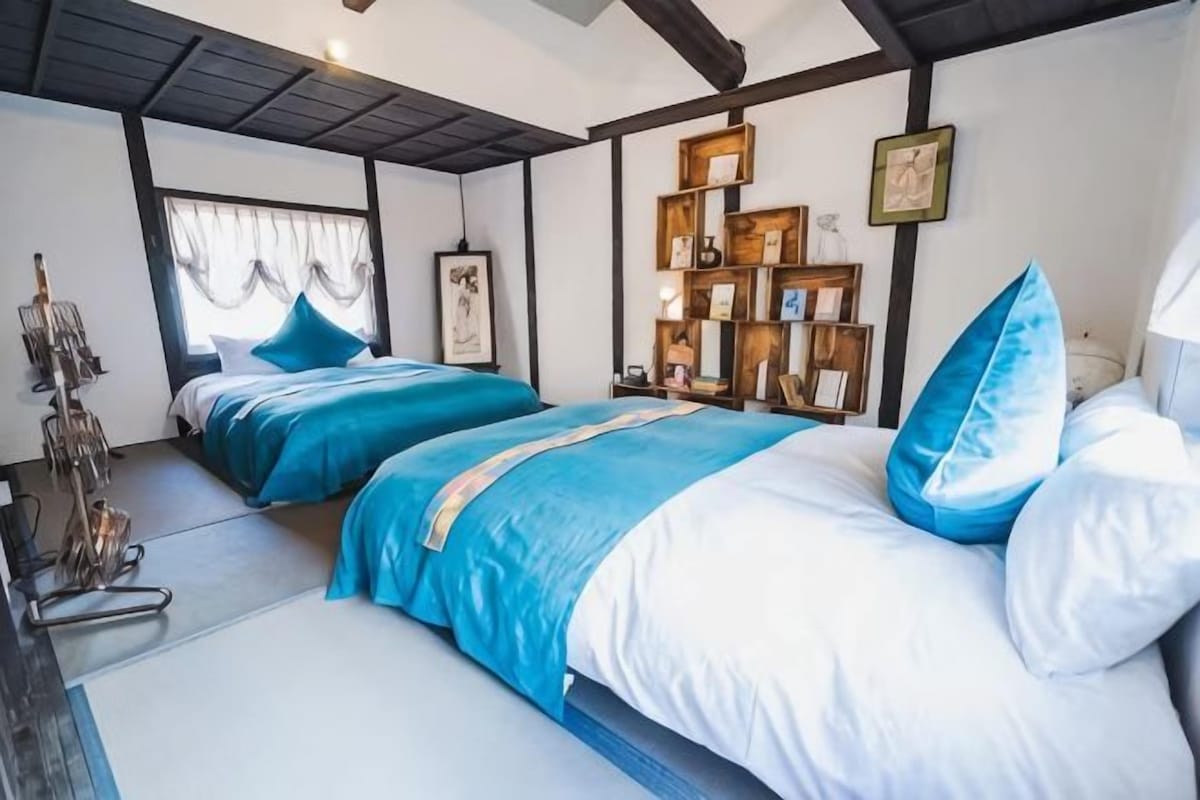 Un dormitorio con dos camas, una estantería y una ventana con cortinas.