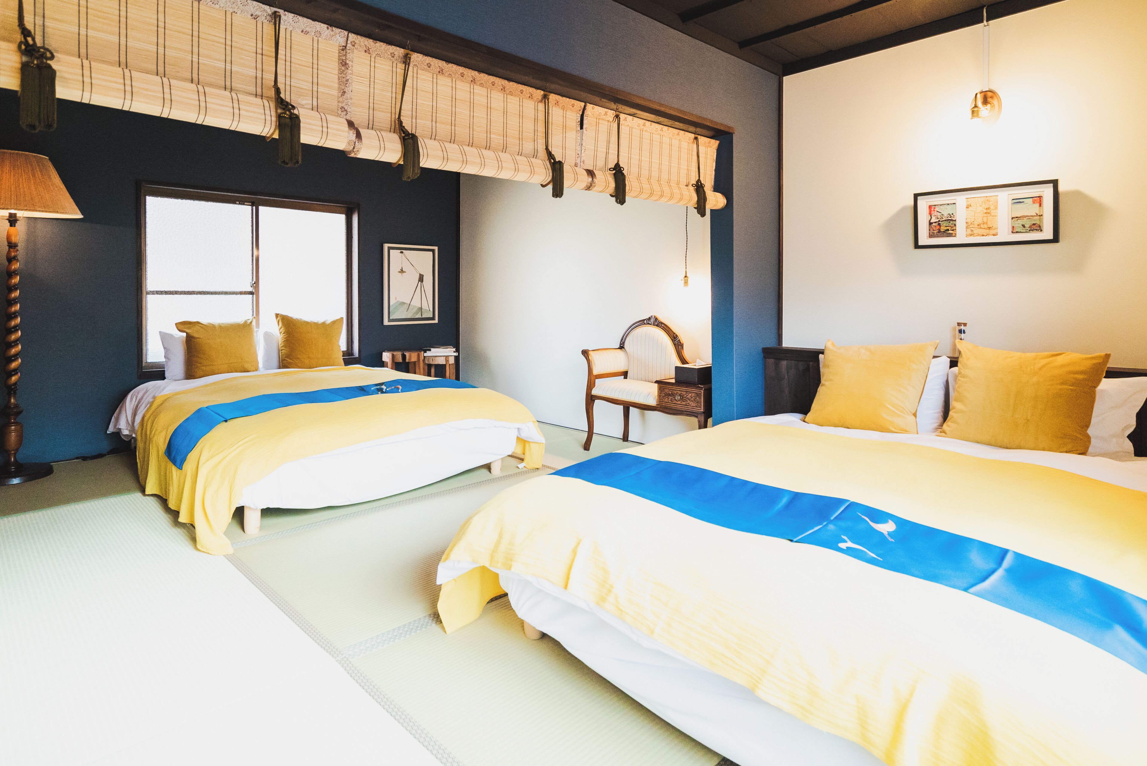 A hotel room with two beds, a large window, a chair, and a lamp.