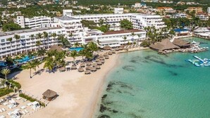 Ein Strandhotel mit mehreren Balkonen, einem Poolbereich und einem Strand mit Sonnenschirmen.