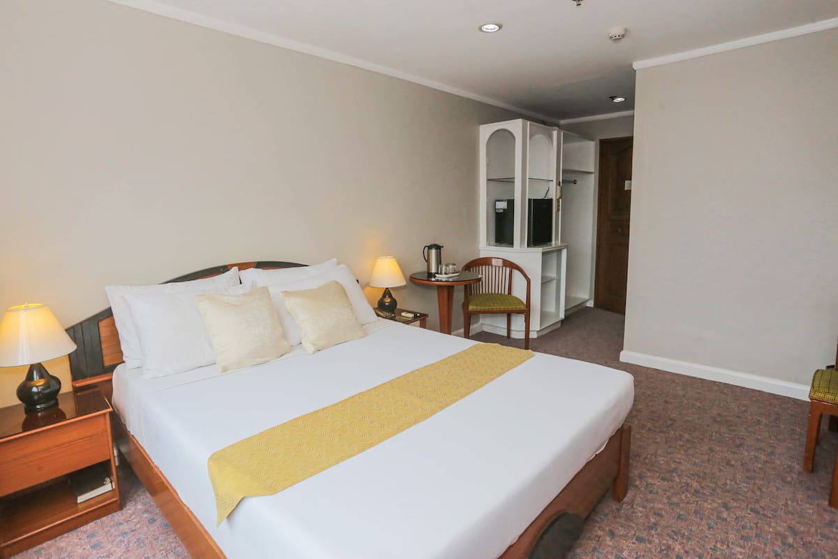 A hotel room with a large bed, bedside lamps, a small table with a lamp, a chair, and a wardrobe.