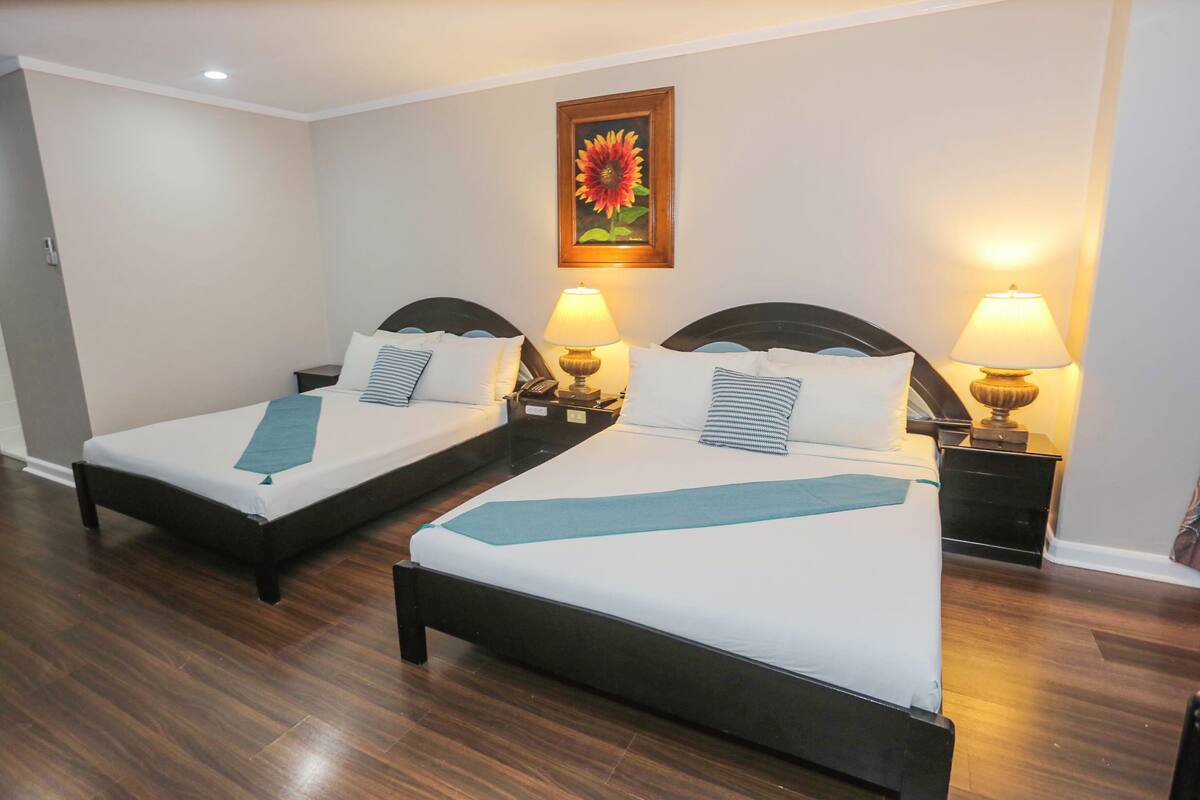 Two single beds with headboards, bedside tables with lamps, a painting of a sunflower on the wall, and wooden flooring.