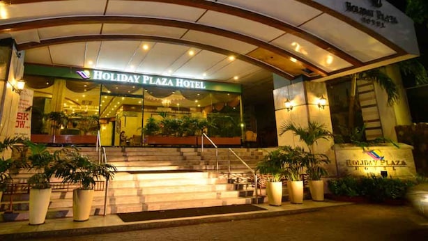 Exterior del Hotel Holiday Plaza, con una entrada destacada, escalones que conducen a ella y plantas en macetas alrededor.