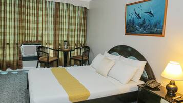 A hotel room with a bed, a desk with two chairs, a painting of dolphins, and a nightstand with a lamp.