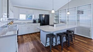 A modern kitchen with white cabinetry, a central island with stools, and a sign that says "eat."