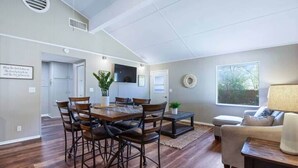 A dining area with a wooden table and chairs, a sofa, and a TV mounted on the wall.