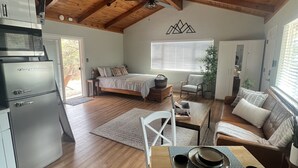 Amplia sala de estar con techo alto, vigas de madera, una mesa de comedor dispuesta con platos, un sofá y una cama con vistas al exterior.