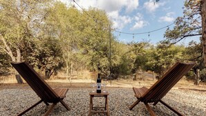 Dos sillones de madera enfrentados, con una mesa pequeña entre ellos, una botella de vino y dos copas de vino sobre la mesa.