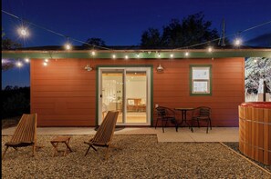 A wooden building with a glass door entrance, outdoor seating with chairs and tables, and string lights above. - Modern Cabin with Private Jacuzzi - Casa de Manzanita (Ahwahnee)