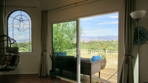 Une pièce dotée d’une porte-fenêtre coulissante donnant sur une terrasse, d’un fauteuil en osier, d’un coussin bleu et d’une plante en pot.
