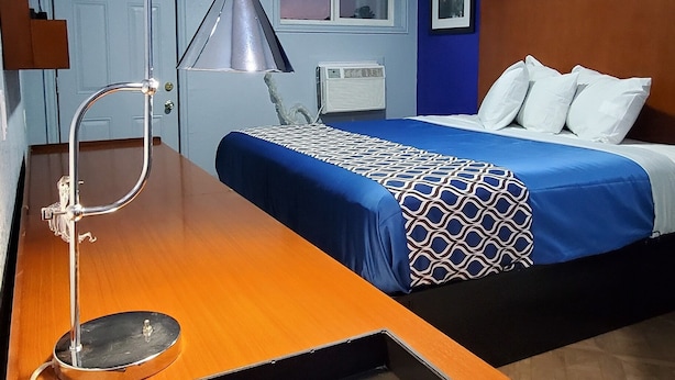 Ein Hotelzimmer mit einem Holztisch, einer Schreibtischlampe, einem Bett mit einem gemusterten Überwurf und einem Fenster mit Blick nach draußen.