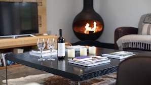 A cozy living room with a fireplace, a bottle of wine, two glasses, and books on a coffee table. - Spring Barn, Chipping Norton - sleeps 4 guests  in 2 bedrooms (Great Rollright)