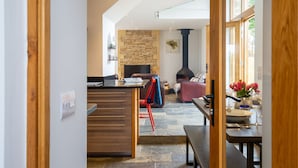 A modern kitchen with a stone backsplash, a dining area with a wooden table, and a cozy living space with a fireplace. - Spring Barn, Chipping Norton - sleeps 4 guests  in 2 bedrooms (Great Rollright)