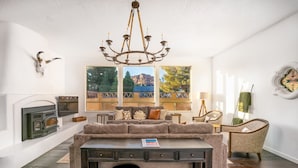 Een gezellige woonkamer met een open haard, een groot raam met een mooi uitzicht, een comfortabele bank en een kroonluchter.