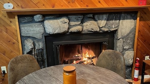 Ein gemütliches Zimmer mit einem Steincheminée, Holzwänden und einem runden Tisch mit einer Kerze.
