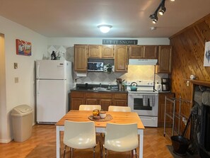 A compact kitchen with wooden cabinets, a white refrigerator, a stove, and a dining table with chairs.
