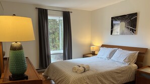 Ein ordentlich eingerichtetes Schlafzimmer mit einem großen Bett, einer Nachttischlampe, einem Bild an der Wand und einem Fenster mit Vorhängen.