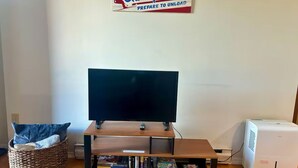 A living room with a flat-screen TV on a wooden stand, a bookshelf with various books, a wicker chair, and a sign on the wall. - Slopeside Condo with indoor fireplace (Hunter)