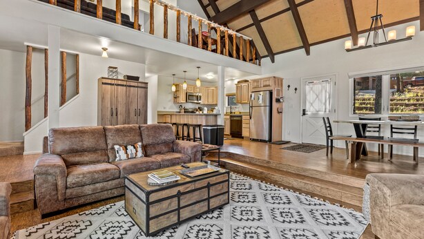 A spacious living area with a high ceiling, wooden beams, a leather sofa, a coffee table, and a dining area with a view of the outdoors. - Flagstaff Bogey Inn! A-Frame cabin Golf Course Lot (Flagstaff)