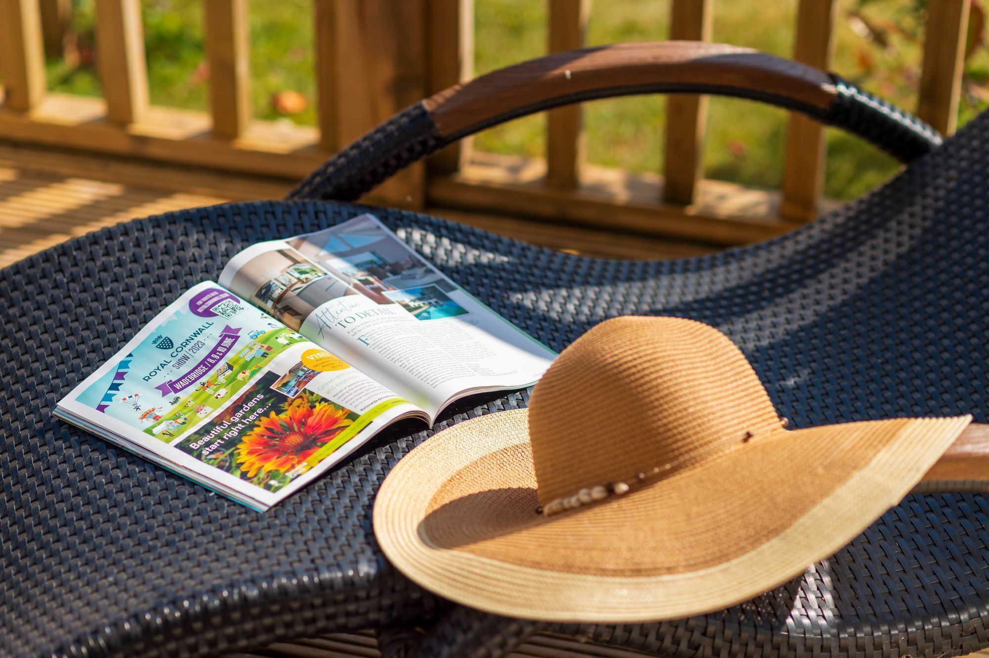 Un magazine posé sur une chaise en osier, avec un chapeau de paille à côté.