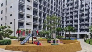 Ein Spielplatz mit Rutschen und Klettergeräten, umgeben von einer kreisförmigen Sandfläche, neben einem mehrstöckigen Gebäude mit Balkonen.