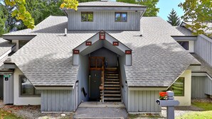 A two-story building with a steeply pitched roof, a central entrance with a staircase, and a mailbox with flowers. - The Woods Resort and Spa Killington: 2 BR / 2 BA Renovated Condos w/ Great Amenities V7 (Killington)