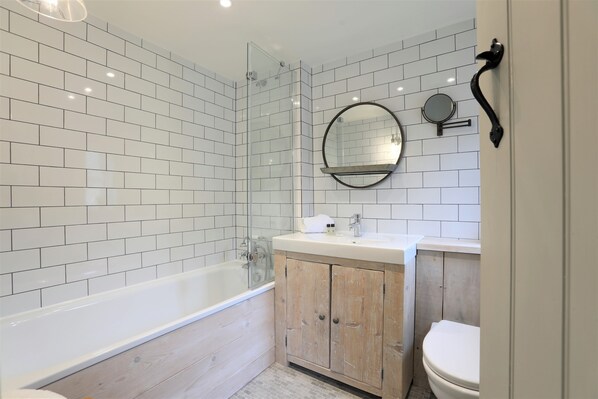 Un baño moderno con azulejos blancos tipo metro, ducha con cerramiento de vidrio, tocador de madera y un espejo redondo.