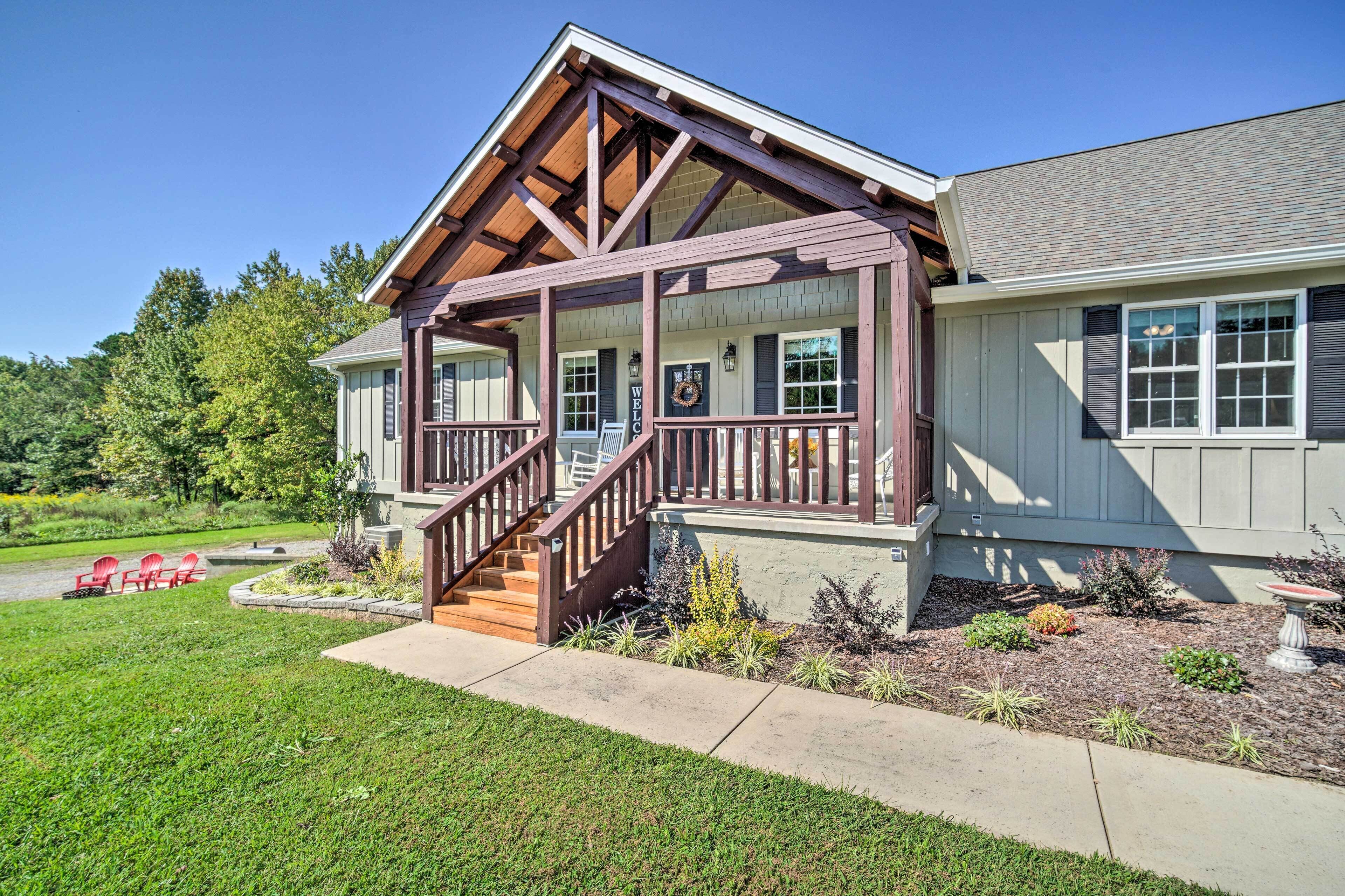 A two-story house with a covered porch, a staircase, and a landscaped front yard with a pathway and red chairs.