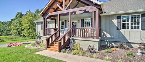 A two-story house with a covered porch, a staircase, and a landscaped front yard with a pathway and red chairs.