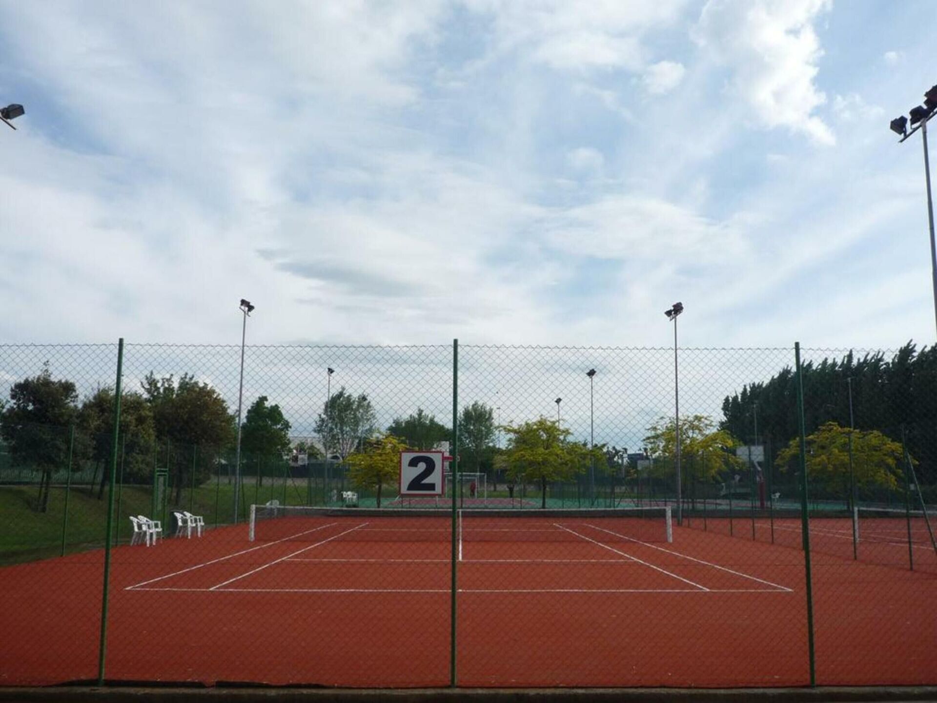 Un court de tennis avec un filet, entouré d’une clôture grillagée, et un panneau indiquant le numéro du court : 2.