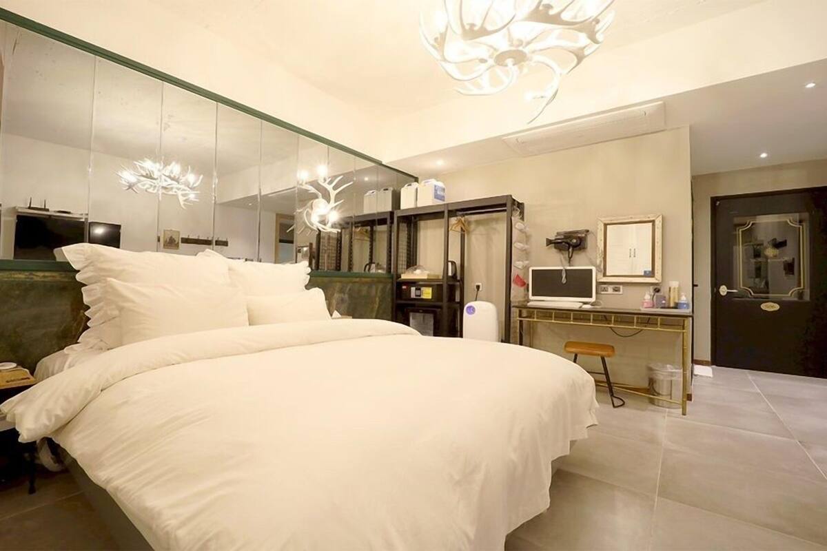 A modern bedroom with a large bed, a desk with a computer, and a mirror.