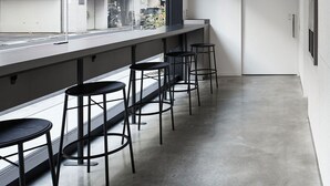 A modern bar area with a long counter and four stools, a large window with a view of buildings, and a concrete floor. - 9h nine hours Ningyocho (Tokyo)