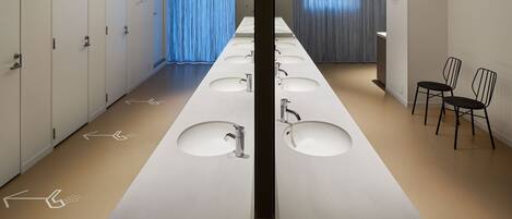 A long, narrow restroom with multiple sinks and a row of lockers on one side.