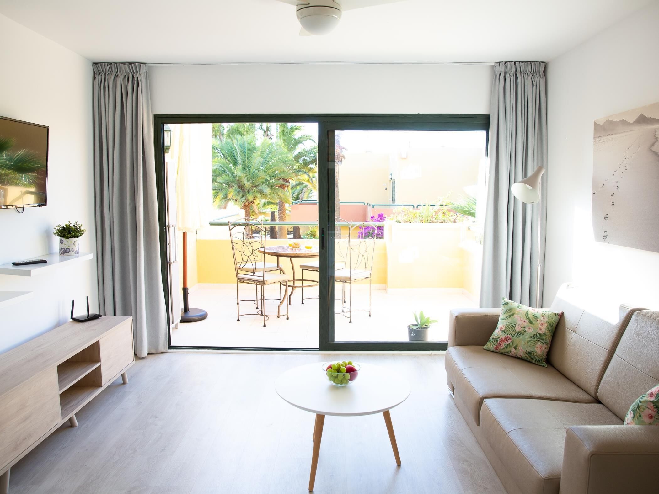 A modern living room with a sofa, a coffee table, a TV, and a balcony with a table and chairs.