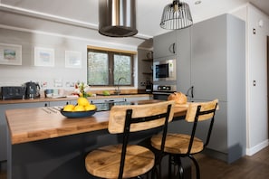 Een moderne keuken met een houten kookeiland, roestvrijstalen apparatuur en een groot raam met zonwering.