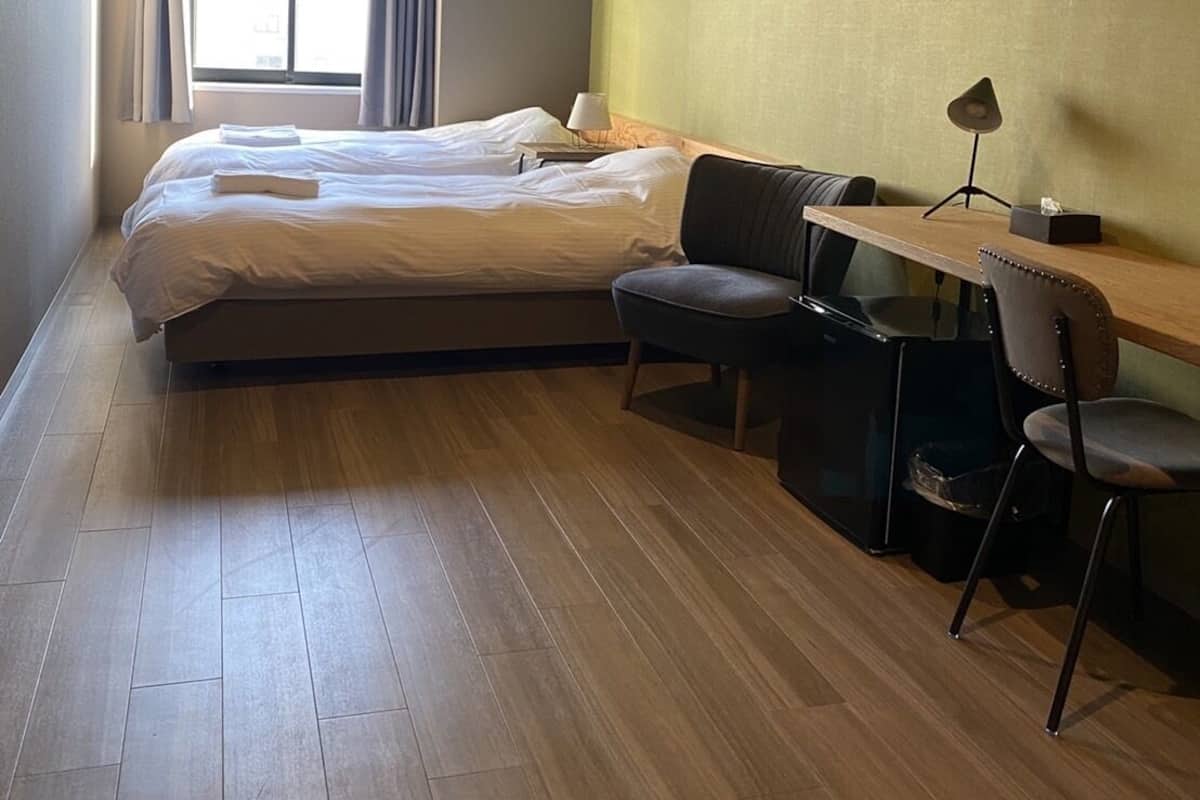 A hotel room with a large bed, a desk with a chair, and a window with curtains.