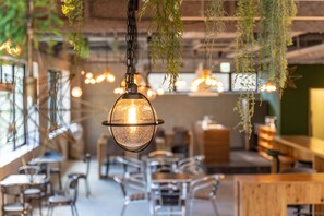 A restaurant interior with hanging plants, pendant lighting, and a modern seating arrangement.