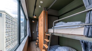 A compact hotel room with bunk beds, a wooden ladder, and a view of a cityscape through large windows. - WISE OWL HOSTELS SAPPORO (Sapporo)