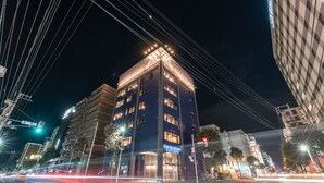 A multi-story hotel with illuminated signage, a crosswalk, and surrounding urban buildings. - WISE OWL HOSTELS SAPPORO (Sapporo)