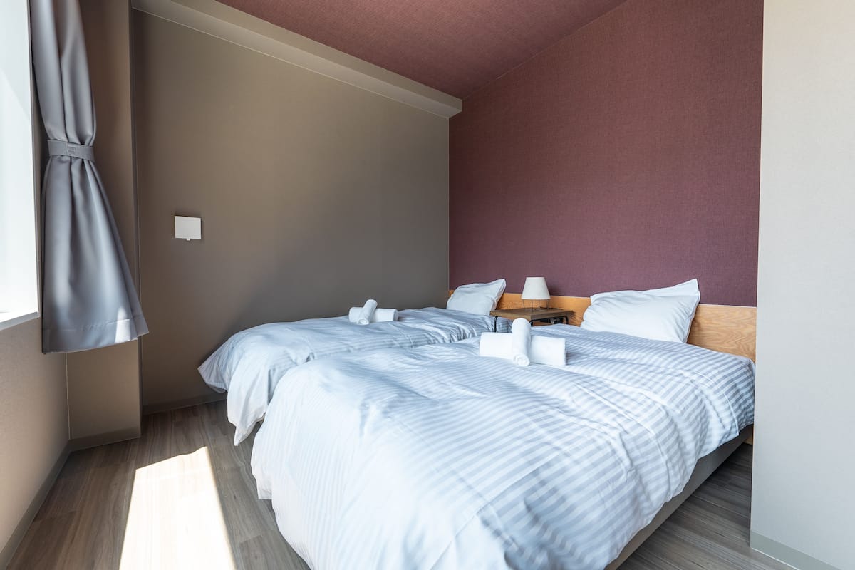 A hotel room with two beds, a wooden nightstand, and a window with a curtain.