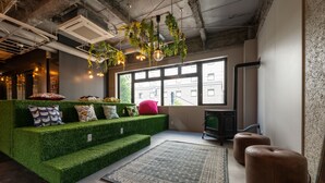 A modern living room with a green artificial grass sofa, a patterned rug, and leather ottomans. - WISE OWL HOSTELS SAPPORO (Sapporo)