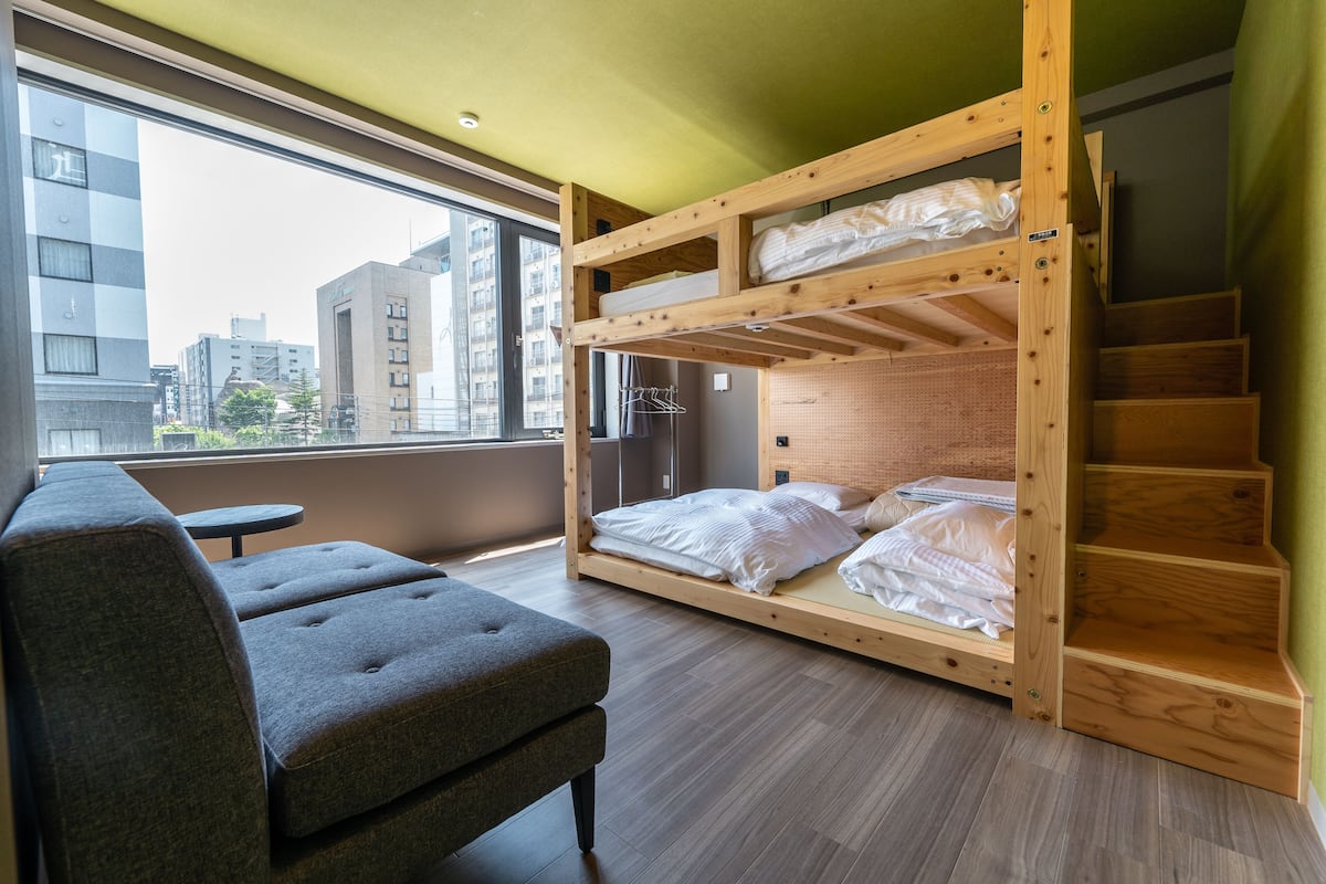 A bunk bed room with a view of the city, a grey sofa, and a small table.