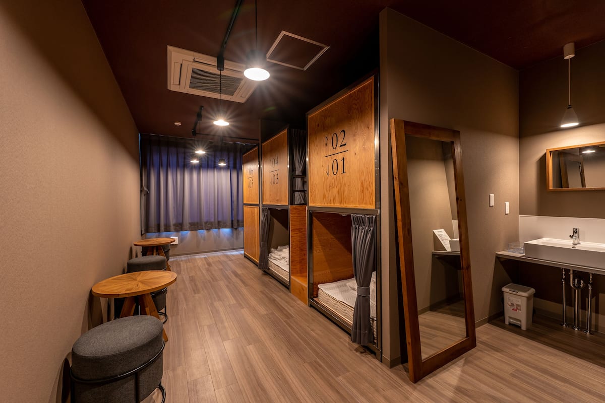 A hotel room with bunk beds, a small table, a mirror, and a sink.