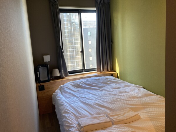 A hotel room with a bed, a desk, a lamp, and a window with curtains.