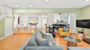 A spacious living area with a sofa, dining table, and chairs, a kitchen in the background, and a TV on a stand.