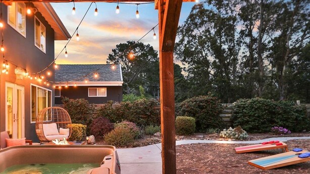 A backyard with a hot tub, string lights, a swing chair, and a deck with lounge chairs.