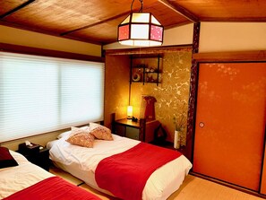 A hotel room with two beds, a wooden ceiling, a wall-mounted shelf with decorative items, and a door. - TSUDOYA Tsukamoto (Osaka)