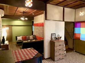 A cozy room with a checkered table, a sofa with patterned cushions, a wooden dresser, and a staircase with colorful curtains. - TSUDOYA Tsukamoto (Osaka)
