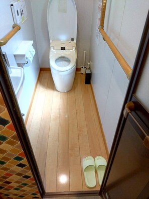 A small, narrow bathroom with a toilet, a sink, and a pair of slippers on the floor. - TSUDOYA Tsukamoto (Osaka)
