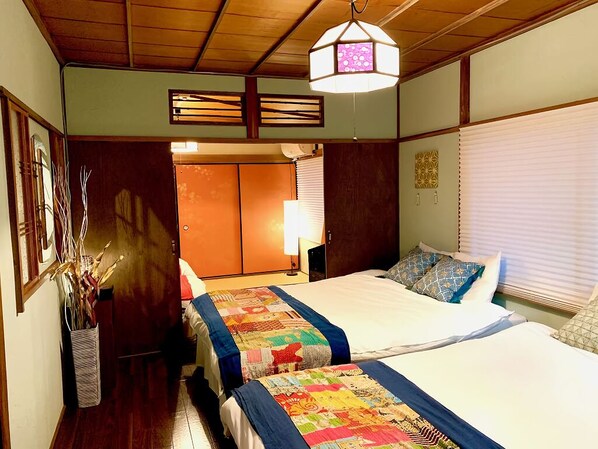 A hotel room with two beds, a wooden ceiling, a hanging light fixture, and a window with blinds. - TSUDOYA Tsukamoto (Osaka)