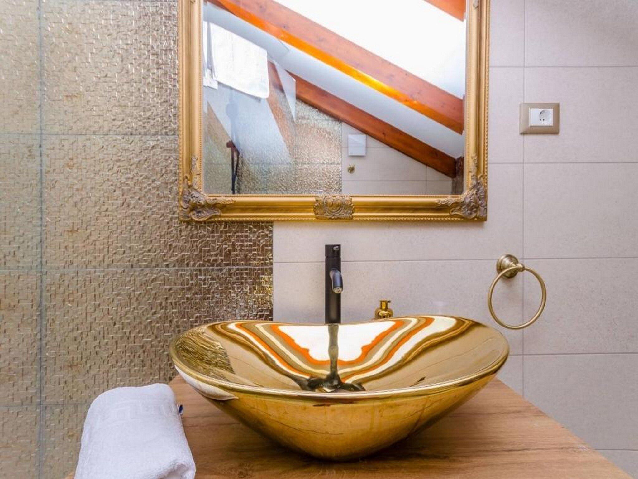 A bathroom with a large, ornate mirror, a unique bowl sink, and a towel on the counter.